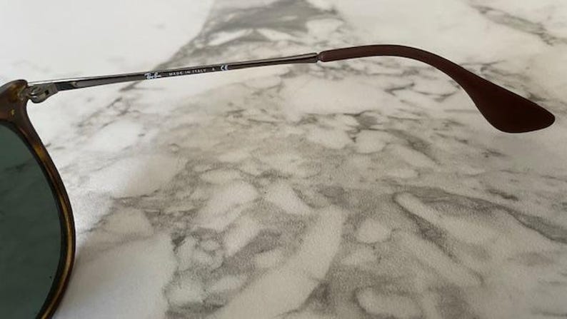 K&ouml;nnte beinhalten: Nahaufnahme einer Sonnenbrille. Der Rahmen hat ein Schildpattmuster mit dunklen Gl&auml;sern. Der B&uuml;gel ist silberfarben mit dem Text "MADE IN ITALY" und einem braunen Ohrb&uuml;gel.