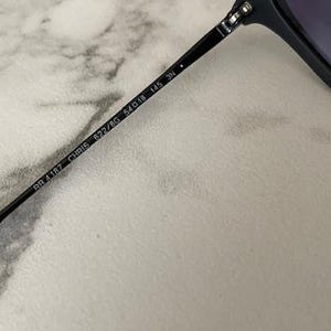 May include: Close-up of a black sunglasses arm with the text "RB 4187 CHRIS 622/8G 54o18 145 3N". The sunglasses arm is black and has a sleek, modern design. The lens is visible in the background.