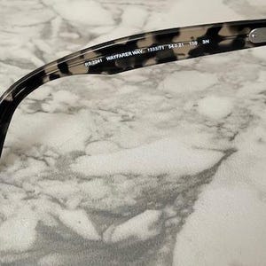 Puede incluir: Primer plano de gafas de sol Wayfarer con un patr&oacute;n de carey en la montura. Las lentes son de color azul oscuro. El texto "RB2141 WAYFARER WAY 1333/71 54 21 150 3N" est&aacute; impreso en la patilla.