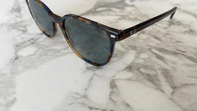 May include: Sunglasses with a tortoiseshell pattern frame and dark lenses. The sunglasses have a classic design with a subtle logo on the temple. The frame is a mix of brown and black.
