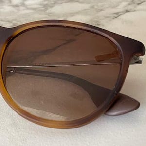 May include: Brown sunglasses with a tortoiseshell pattern on the frames. The lenses are a gradient brown color. The sunglasses have a classic, rounded shape and silver metal accents.