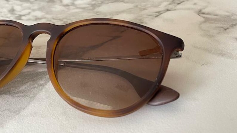 May include: Brown sunglasses with a tortoiseshell pattern on the frames. The lenses are a gradient brown color. The sunglasses have a classic, rounded shape and silver metal accents.