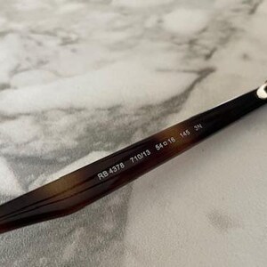 May include: Close-up of sunglasses with a brown and black tortoiseshell pattern on the frame. The text "RB 4378 710/13 54o16 145 3N" is printed on the arm of the sunglasses. The lenses are brown.