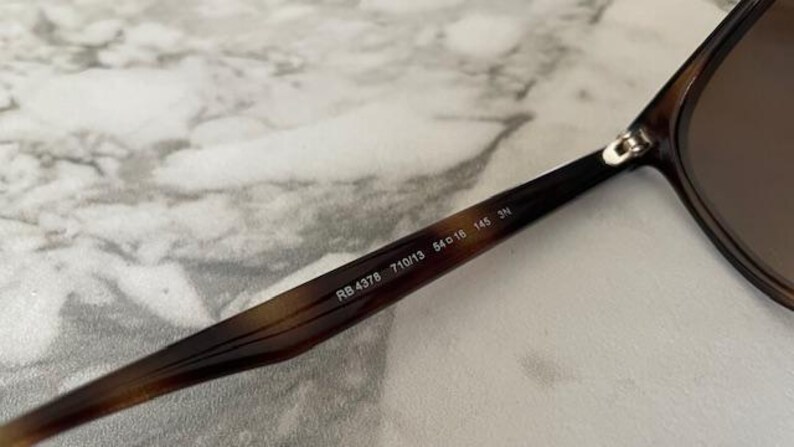 May include: Close-up of sunglasses with a brown and black tortoiseshell pattern on the frame. The text "RB 4378 710/13 54o16 145 3N" is printed on the arm of the sunglasses. The lenses are brown.