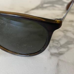K&ouml;nnte beinhalten: Nahaufnahme einer Sonnenbrille mit dunklen Gl&auml;sern und einem Schildpattrahmen. Die Sonnenbrille hat ein klassisches Design mit einer leicht abgerundeten Form. Der Rahmen ist eine Mischung aus Braun- und Bernsteint&ouml;nen.