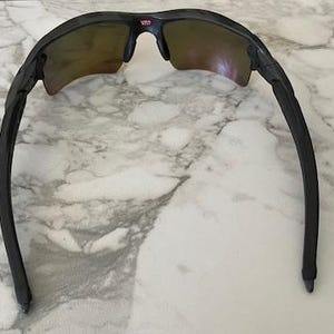 Peut inclure: Lunettes de soleil noires avec une monture incurv&eacute;e et des verres teint&eacute;s. Le haut de la monture pr&eacute;sente un petit d&eacute;tail rouge et blanc. Les lunettes sont con&ccedil;ues pour le sport ou les activit&eacute;s de plein air.