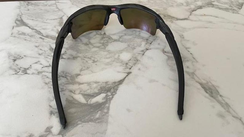 Peut inclure: Lunettes de soleil noires avec une monture incurv&eacute;e et des verres teint&eacute;s. Le haut de la monture pr&eacute;sente un petit d&eacute;tail rouge et blanc. Les lunettes sont con&ccedil;ues pour le sport ou les activit&eacute;s de plein air.