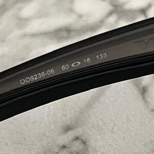 May include: Close-up of a black eyeglass frame with the model number OO9236-06, lens width 60 mm, bridge width 16 mm, and temple length 133 mm. The brand name is partially visible.