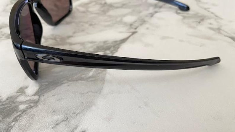 May include: Black sunglasses with a curved frame and dark lenses. The sunglasses have a glossy finish and a small logo on the temple. The design is sleek and modern, suitable for outdoor activities.