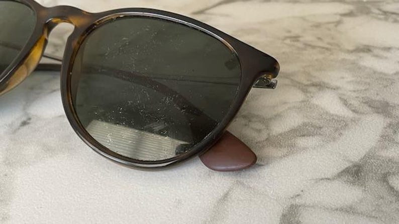 K&ouml;nnte beinhalten: Nahaufnahme einer Sonnenbrille mit Schildpattrahmen und dunklen Gl&auml;sern. Die Sonnenbrille hat eine klassische runde Form und braune B&uuml;gel. Die Gl&auml;ser scheinen zerkratzt zu sein. Die Sonnenbrille liegt auf einer hellen Oberfl&auml;che.