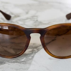 May include: Brown tortoiseshell sunglasses with a rounded frame and gradient lenses. The Ray-Ban logo is visible on the left lens. The temples are brown and the arms are silver.