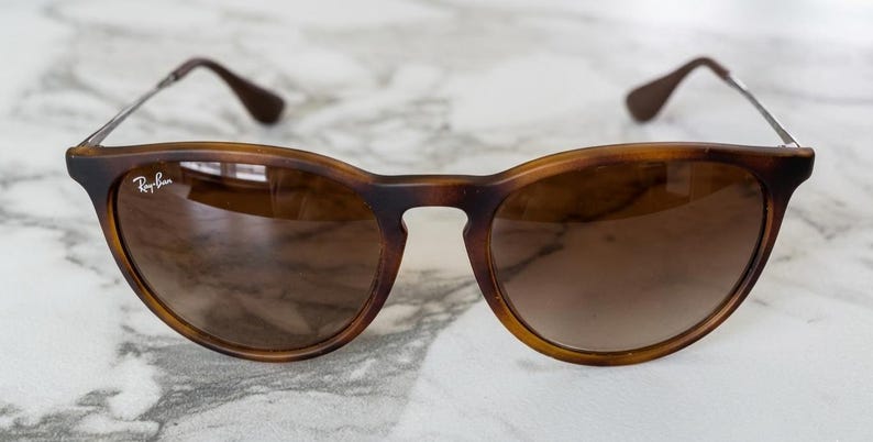 May include: Brown tortoiseshell sunglasses with a rounded frame and gradient lenses. The Ray-Ban logo is visible on the left lens. The temples are brown and the arms are silver.