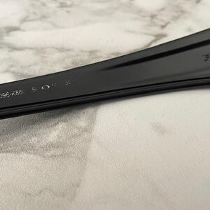 May include: Close-up of a black sunglasses arm. The text "FUEL CELL" is visible on the arm. The model number "OO9096-K66" and other markings are also present. The sunglasses arm is made of a smooth, matte material.