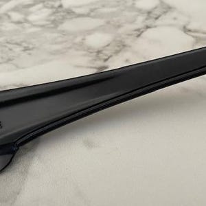 May include: Close-up of a black sunglasses arm. The arm is sleek and glossy, with a small, reflective silver accent near the temple. The frame has a subtle curve and a CE marking.