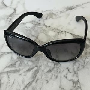 K&ouml;nnte beinhalten: Schwarze Sonnenbrille mit geschwungenem Rahmen und dunklen Gl&auml;sern. Die Sonnenbrille hat eine subtile Cat-Eye-Form und das Ray-Ban-Logo ist auf dem linken Glas sichtbar. Auf einem Marmorhintergrund.