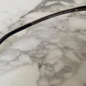 May include: Close-up of sunglasses with a dark frame and gradient lenses. The temple arm is black with text that reads "RB 3045 WARRIOR 204/51 60[]12 2N". The sunglasses are resting on a marble surface.