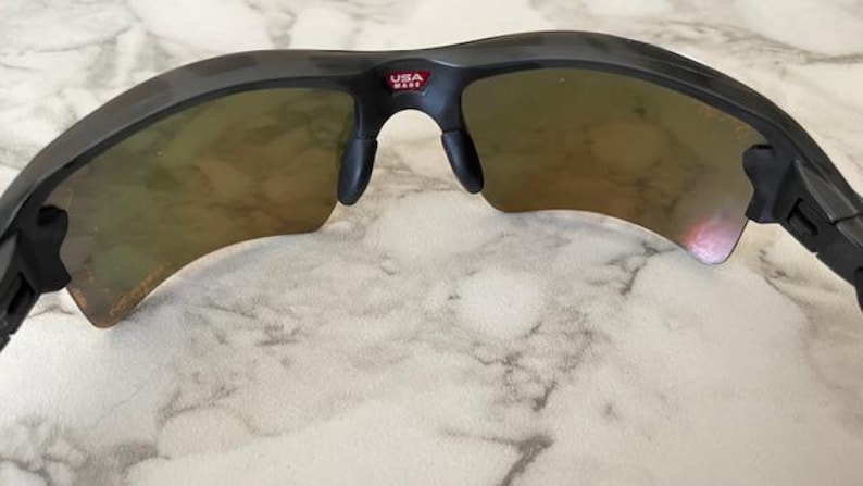 Peut inclure: Lunettes de soleil de sport noires avec des verres teint&eacute;s orange. Les lunettes ont une monture incurv&eacute;e et des plaquettes de nez. Le texte "USA MADE" est visible sur la monture. Ces lunettes sont con&ccedil;ues pour les activit&eacute;s de plein air.