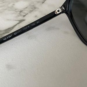 Puede incluir: Gafas de sol negras con dise&ntilde;o de aviador cl&aacute;sico. La montura negra tiene el texto "RB 4387 601/71 56o18 145 3N" impreso en la patilla. Las lentes oscuras contrastan con un fondo claro. Dise&ntilde;o cl&aacute;sico.