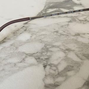 K&ouml;nnte beinhalten: Nahaufnahme einer Sonnenbrille mit braun-schwarzem Schildpattrahmen und dunklen Gl&auml;sern. Der B&uuml;gel ist braun und verj&uuml;ngt sich zu einer abgerundeten Spitze. Das Metallscharnier und der B&uuml;gel sind sichtbar.