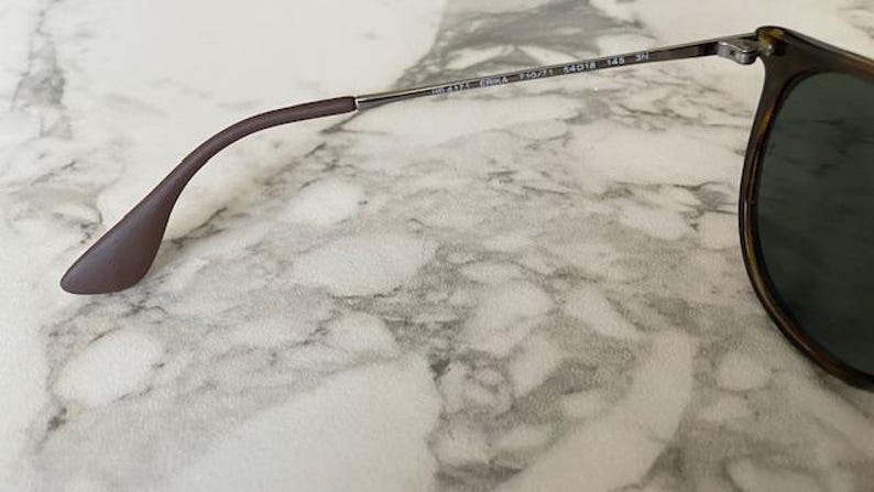K&ouml;nnte beinhalten: Nahaufnahme einer Sonnenbrille mit braun-schwarzem Schildpattrahmen und dunklen Gl&auml;sern. Der B&uuml;gel ist braun und verj&uuml;ngt sich zu einer abgerundeten Spitze. Das Metallscharnier und der B&uuml;gel sind sichtbar.