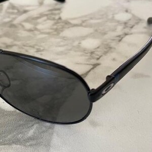May include: Black aviator sunglasses with dark tinted lenses. The sunglasses have a sleek, modern design with a metal frame and curved temples. The lenses are oval-shaped and provide full coverage. The sunglasses are suitable for outdoor activities.