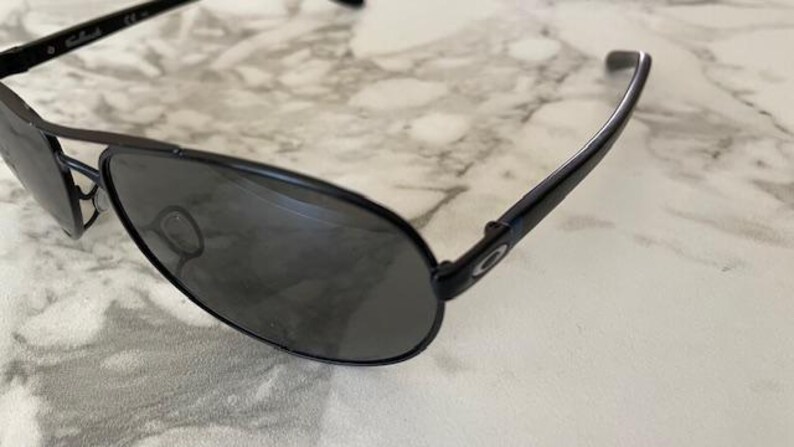 May include: Black aviator sunglasses with dark tinted lenses. The sunglasses have a sleek, modern design with a metal frame and curved temples. The lenses are oval-shaped and provide full coverage. The sunglasses are suitable for outdoor activities.