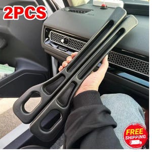 May include: Two black car interior door handle covers. The covers have a textured surface and a long, rectangular shape with a handle opening at the end. The text "2PCS" is in the upper left corner.