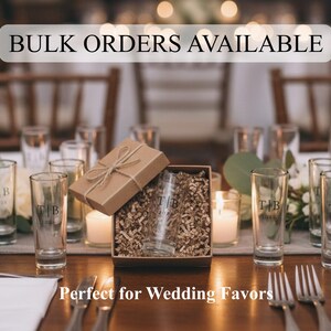 May include: Clear glass shot glasses with the engraved letters T|B and the year 2024. One glass is inside a brown cardboard gift box filled with paper filler, tied with twine. The text BULK ORDERS AVAILABLE and Perfect for Wedding Favors is visible.