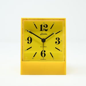 Puede incluir: Un despertador Linden amarillo vintage con números y manecillas negras. La esfera del reloj muestra la palabra "Alarm" y la marca "Linden". El reloj está hecho en Alemania.