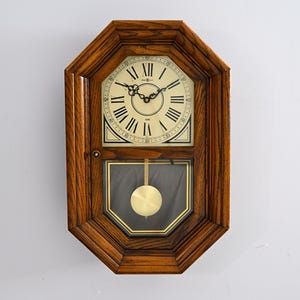 May include: A wooden wall clock with a light-colored face and black Roman numerals. The clock has a pendulum and a dark brown, octagonal frame. The clock hands are black.