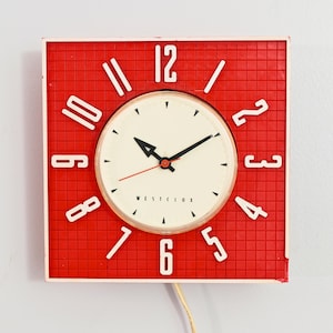 May include: A vintage square wall clock with a red grid-patterned face and a white border. The clock face is cream-colored with black hands and white numerals. The brand name "WESTCLOX" is printed on the face.