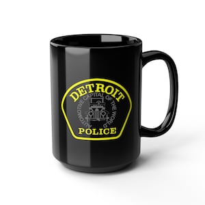 May include: Black ceramic mug featuring the Detroit Police logo in yellow and gray. The logo includes the text "DETROIT AUTOMOTIVE CAPITAL OF THE WORLD POLICE" around an image of a vintage car.