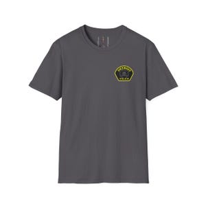 May include: A charcoal gray t-shirt featuring a Detroit Police badge on the upper left chest. The badge is yellow and black, with the words "DETROIT" and "POLICE" in a circular design. The shirt has a crew neck and short sleeves.