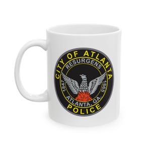 May include: White ceramic mug featuring the Atlanta Police Department emblem. The emblem is a circular design with a phoenix, the words "City of Atlanta Resurgens" and "Police". The mug has a curved handle.