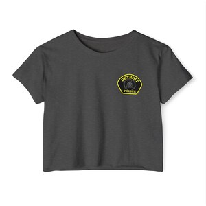 May include: Dark gray crop top with a crew neck. The shirt features a Detroit Police patch on the left chest. The patch is yellow with black and white detailing and the words "DETROIT POLICE".