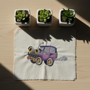 Könnte beinhalten: Ein bestickter Aufnäher mit einem Cartoon-Auto in Lila, Gelb und Orange, mit großen Augen und einer Rauchwolke. Drei kleine Topf-Sukkulenten sind über dem Aufnäher auf einer Holzoberfläche angeordnet.