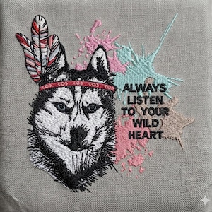 May include: Embroidered image of a husky dog wearing a red headband and feathers. The text "ALWAYS LISTEN TO YOUR WILD HEART" is embroidered in a stylized font with pink, blue, and tan accents on a gray background.