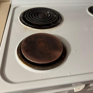 May include: Close-up of a white electric stove top with two burners. One burner has a black, circular heating element. The other burner has a round, brown heating element. The stove top has a white surface.