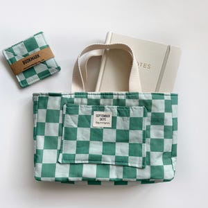 Könnte beinhalten: Eine grün-weiß karierte Tragetasche mit passendem Lesezeichen und Notizbuch. Die Tragetasche hat eine Vordertasche mit einem Etikett mit der Aufschrift "SEPTEMBER SKYE". Das Notizbuch hat das Wort "NOTES" auf dem Einband aufgedruckt.