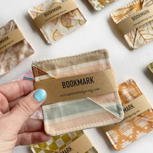 May include: A collection of fabric bookmarks with different patterns, including lemons, flowers, and stripes. Each bookmark has a brown paper tag with the word "BOOKMARK" and a website address.