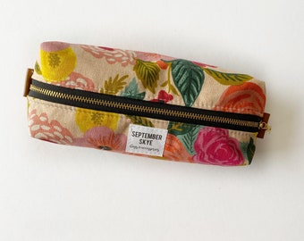 May include: A floral patterned pencil case with a black zipper and a label that reads "SEPTEMBER SKYE  goods & accessories".