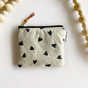 May include: A small beige zippered pouch with a black and white heart pattern. The pouch has a brown leather zipper pull and a white label that says "SEPTEMBER SKYE".