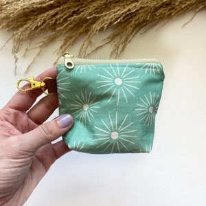 Puede incluir: Una pequeña bolsa de cremallera de color turquesa con un patrón de estrellas blancas y un llavero dorado.