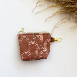 Puede incluir: Una pequeña bolsa de cremallera marrón con un patrón geométrico blanco. La bolsa tiene una cremallera dorada y un llavero dorado.