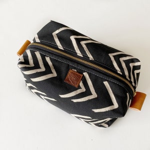 May include: Black canvas toiletry bag with a white chevron pattern and brown leather accents. The bag has a zipper closure and a leather tag with the initials "G.S."