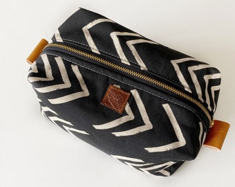 May include: Black canvas toiletry bag with a white chevron pattern and brown leather accents. The bag has a zipper closure and a leather tag with the initials "G.S."