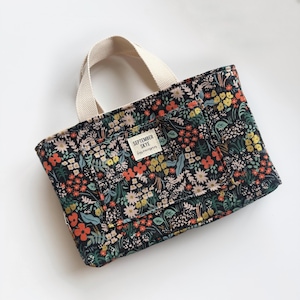 Peut inclure: Un sac fourre-tout en toile noire avec un imprimé floral et une anse en toile blanche. Le sac a une petite poche sur le devant avec le texte "SEPTEMBER SKYE" et "Happy Everything" imprimé dessus.