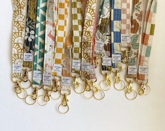 Könnte beinhalten: Eine Sammlung von 10 bunten Stoffschlüsselanhängern mit goldenen Schlüsselringen. Jeder Schlüsselanhänger hat ein anderes Muster und enthält den Text "SEPTEMBER SKYE".