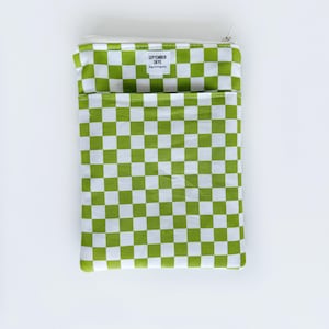 May include: A rectangular, green and white checkered pouch with a zipper closure. The pouch has a pocket on the front and a small white tag with the text "SEPTEMBER SKYE" on it. The pouch is on a white background.