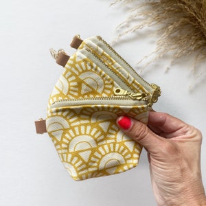 May include: A small, yellow and white patterned pouch with two zipper closures. The pouch is made of fabric and has a geometric sunburst design.